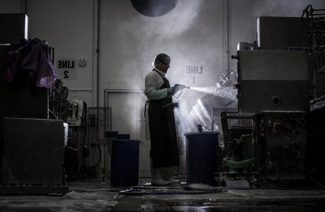 工人穿着防护服喷洒工业设备清洁, 在黑暗和充满蒸汽的环境中